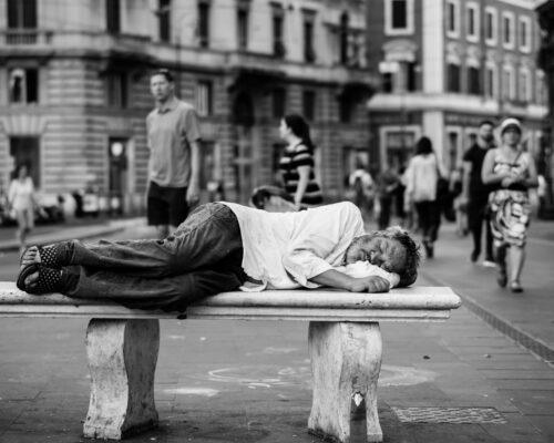 man sleeping on bench in the middle of the street